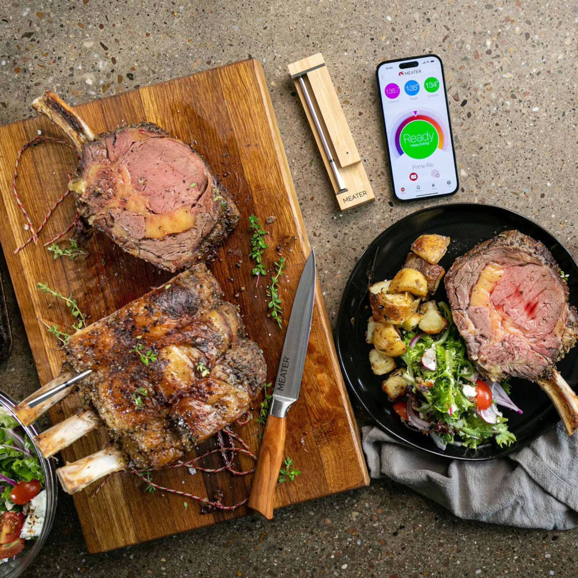 Meater 2 Plus trådløs grilltermometer og repeater ved siden af smartphone med app, synlig bøf og urter.