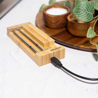 Meater Pro Duo trådløs wifi stegetermometer oplades i bambusblok på køkkenbord med grønne planter og små træskåle.