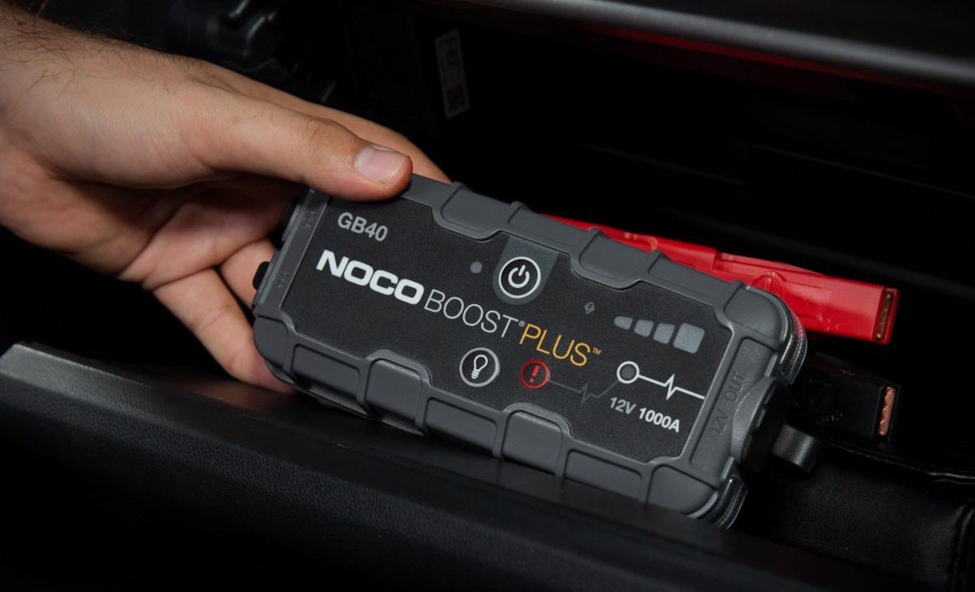 Noco Boost Plus GB40 starthjælp til bil med fastmonterede startkabler ses i et bilrum til 12V nødstart.