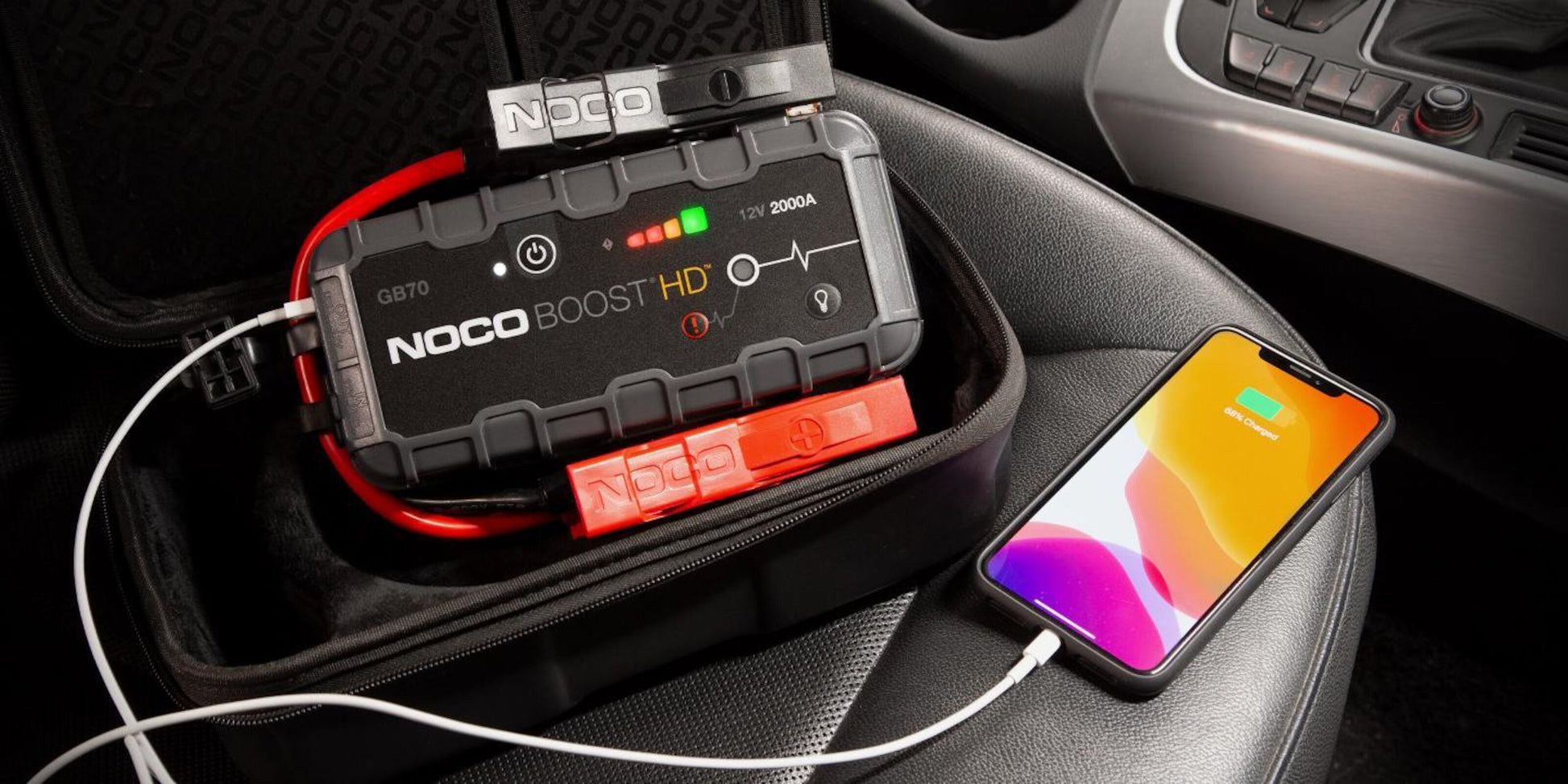Noco Boost Plus GB70 startkabler oplader smartphone via USB, indikatorlys tændt, telefonskærm viser opladning.