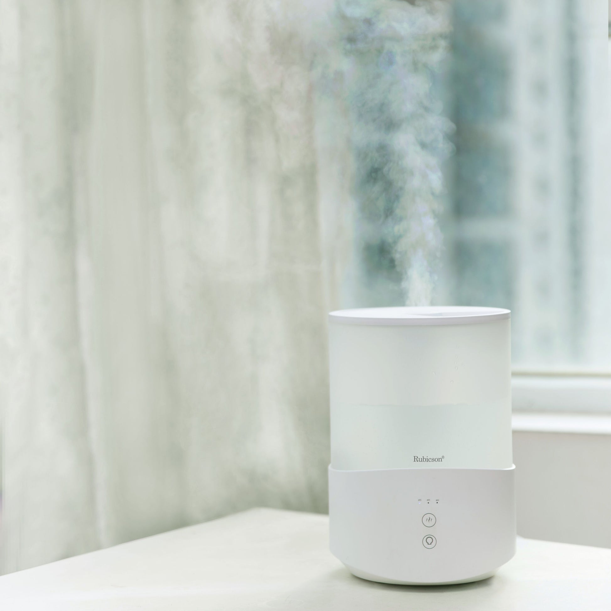 Rubicson luftfugter med timer og stemningsbelysning 2,5 L udsender synlig fugt, placeret ved vindue.