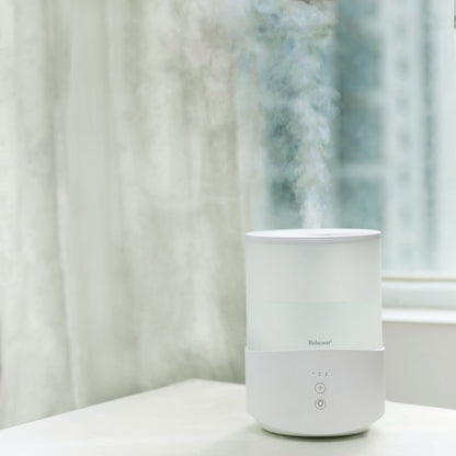 Rubicson luftfugter med timer og stemningsbelysning 2,5 L udsender synlig fugt, placeret ved vindue.