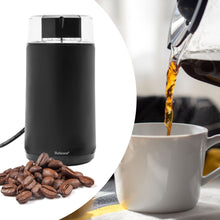 Rubicson Kaffe- og kryddemølle sort rustfrit stål med kaffebønner ved siden af, glas kande hælder kaffe i hvid kop.