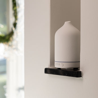 Ultralyd aromadiffuser på sort hylde i vægniche oplyst af sollys.