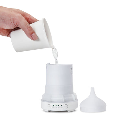 Aromadiffuser med ultralyd, låg ved siden af, vand hældes fra hvid kop i reservoiret, klar til æteriske olier.