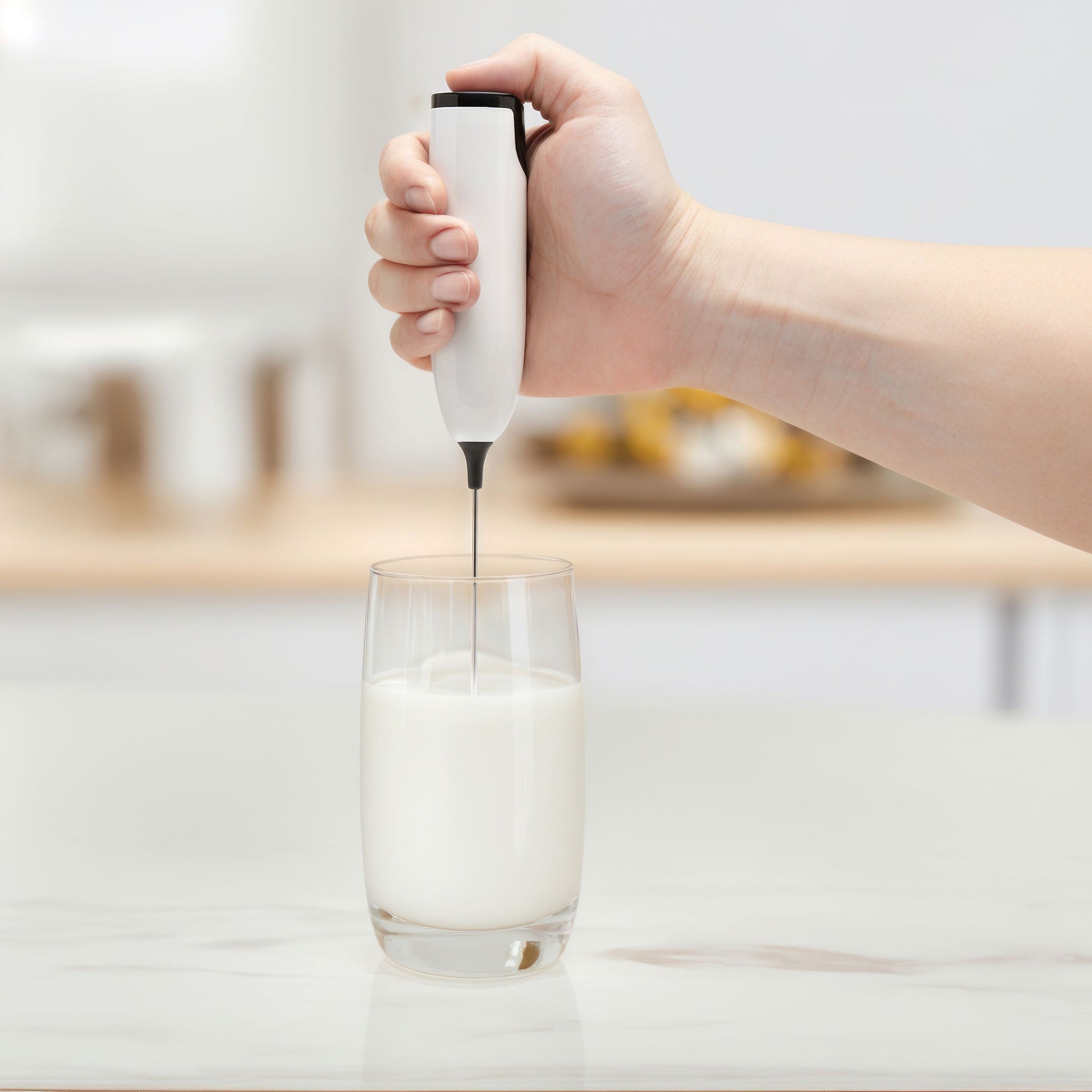 Rubicon batteridrevet mælkeskummer med metalpisker, håndholdt over glas med skummet mælk.