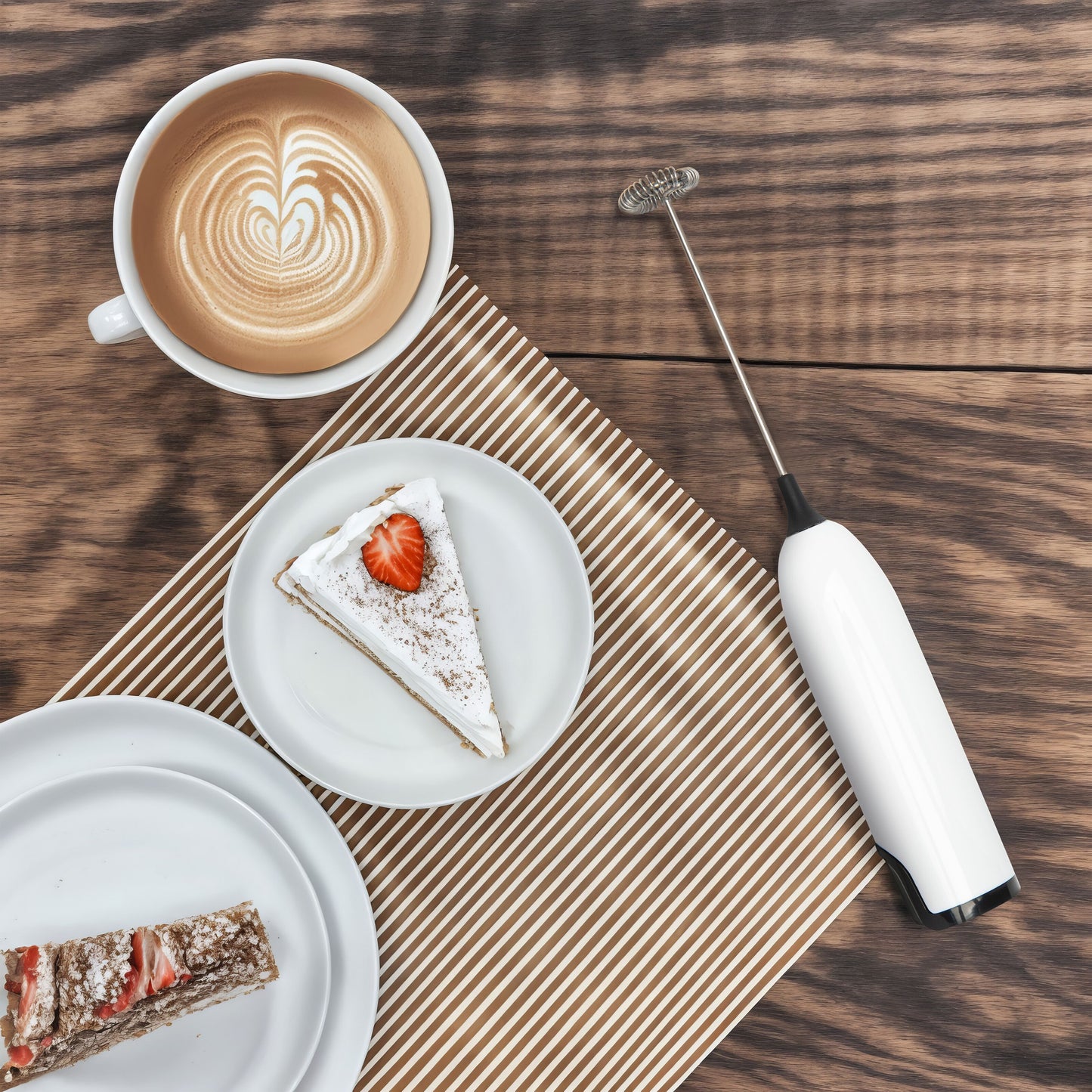 Rubicson batteridrevet mælkeskummer ved siden af latte og jordbærkage på træbord, sort håndtag, kompakt design.