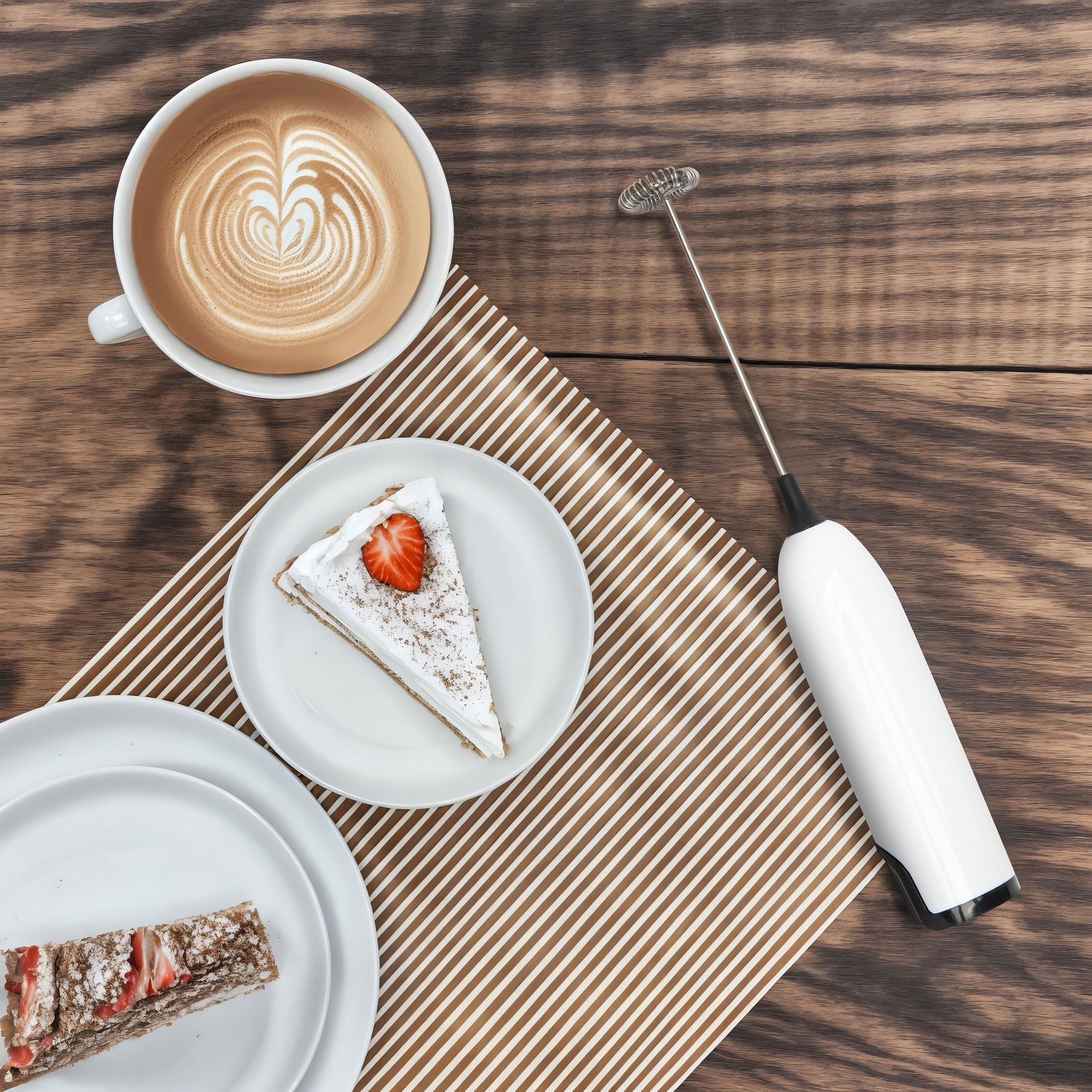 Rubicson batteridrevet mælkeskummer ved siden af latte og jordbærkage på træbord, sort håndtag, kompakt design.
