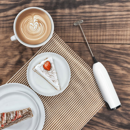 Rubicson batteridrevet mælkeskummer ved siden af latte og jordbærkage på træbord, sort håndtag, kompakt design.