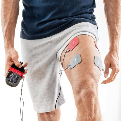 Beurer EM 59 TENS/EMS muskelstimulator med varme på lår, fire elektrodepuder tilsluttet håndholdt enhed.