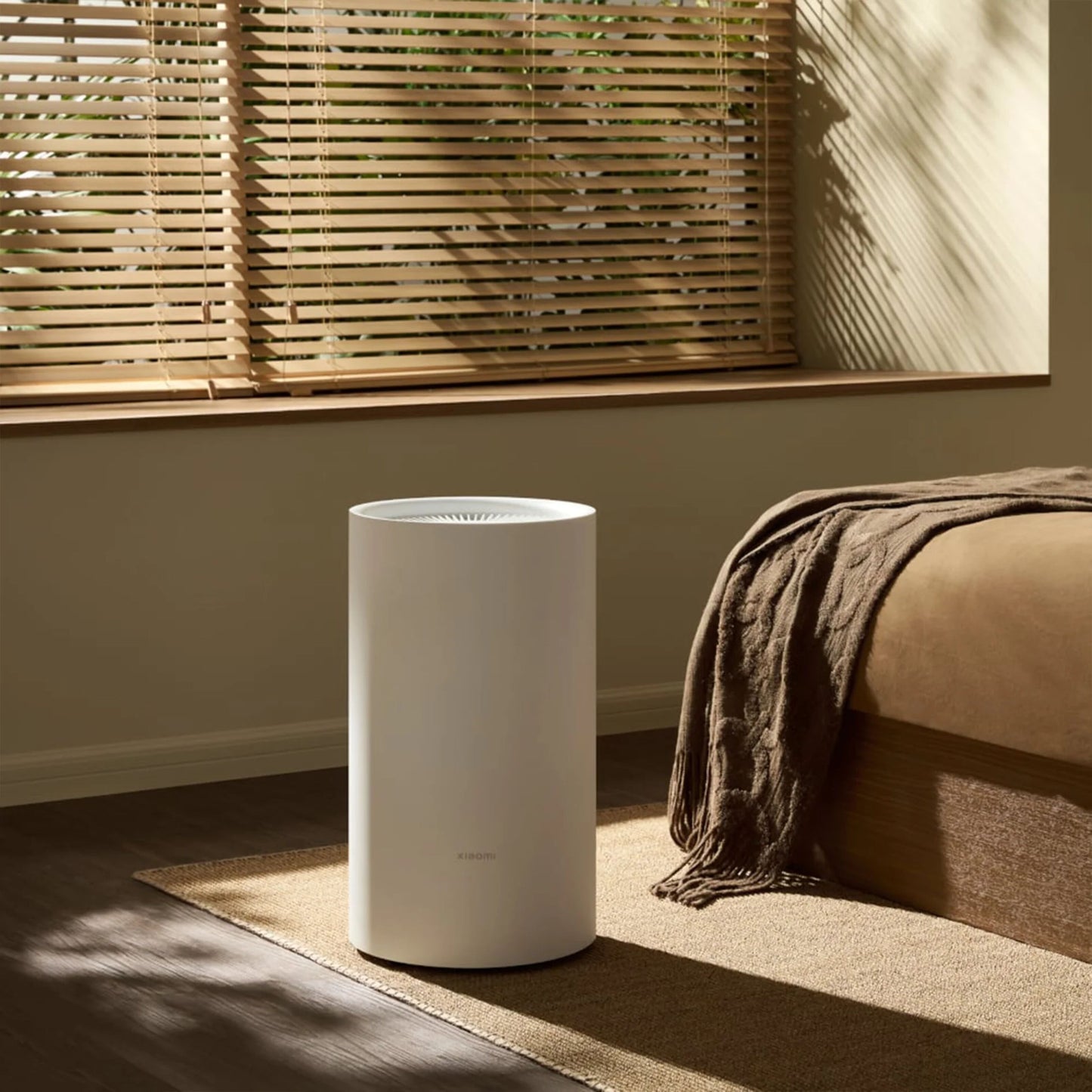 Xiaomi Smart Affugter Lite 13 l/døgn på brunt tæppe ved seng med brun plaid i lyst rum med persienner.