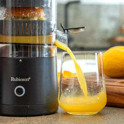 Rubicson bærbar citruspresser presser juice i klart glas på køkkenbord med friske appelsiner ved siden af.