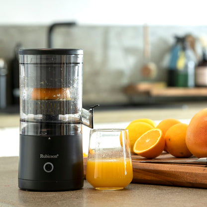 Rubicson Bærbar citruspresser sort med klar beholder ved siden af friskpresset juice og flere hele/halve appelsiner på træbræt.