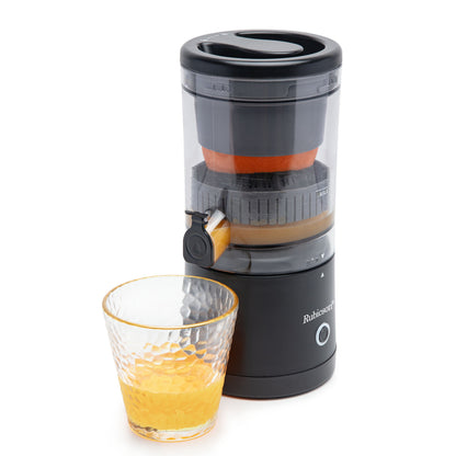 Bærbar citruspresser sort, transparent låg med synlig frugt, frisk juice løber ned i lille glas med appelsinjuice.