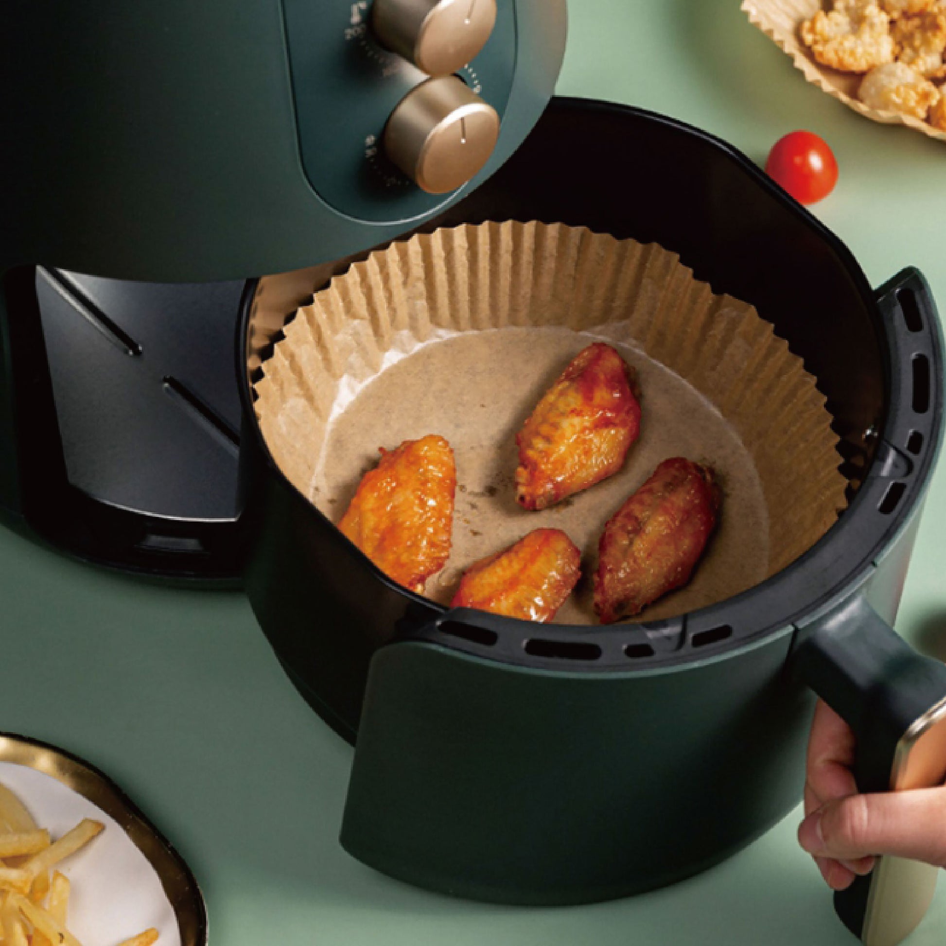 Rubicson Airfryer papirark 50-pak fjernes fra kurv med fire kyllingevinger, pommes frites og cherrytomat ved siden af.