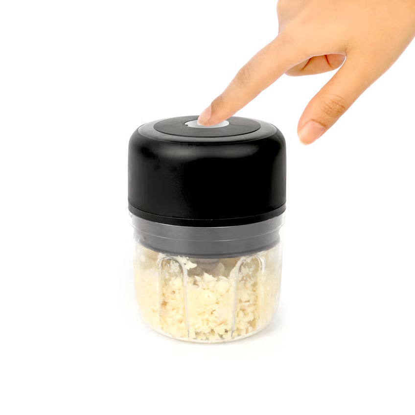 Hånden trykker på knappen øverst på den trådløse mini-hakker til grøntsager og frugt, der er fyldt med hakket hvidløg.