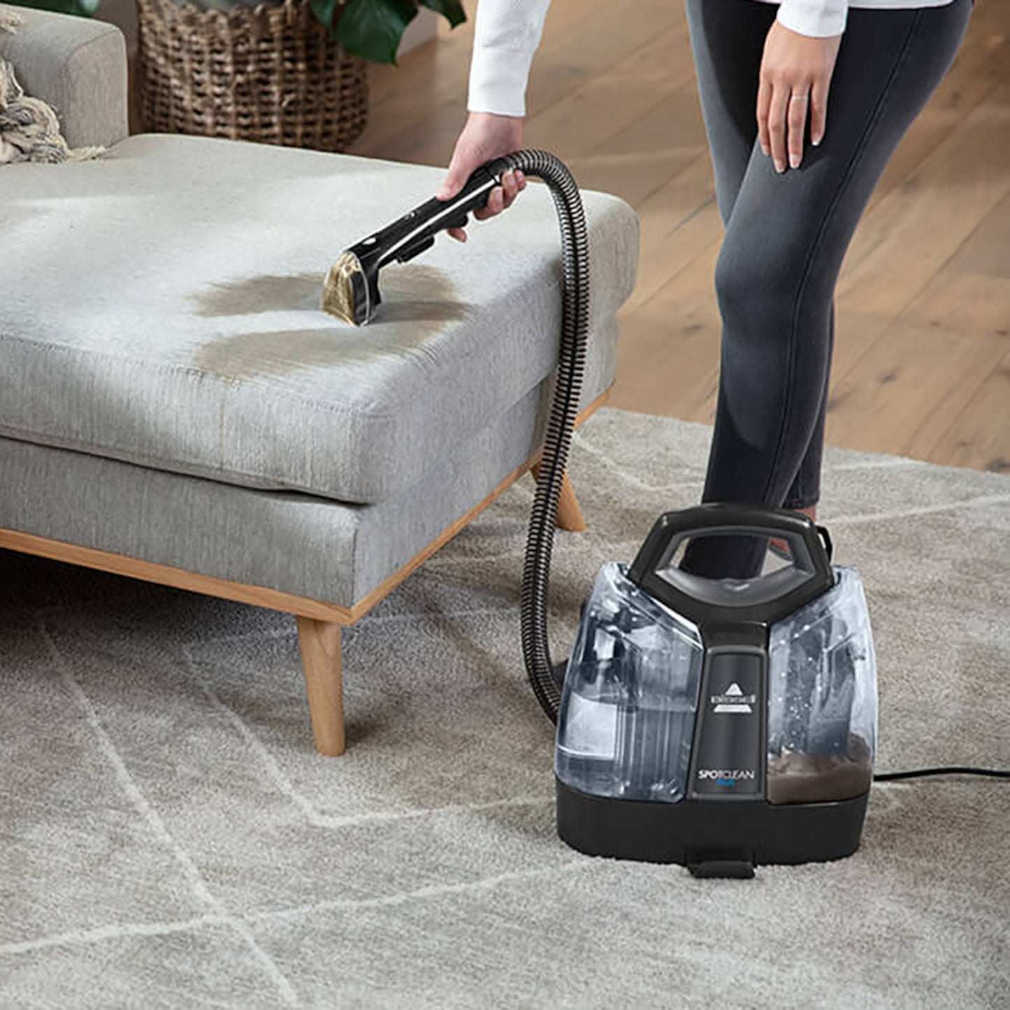 Bissel SpotClean Plus tæppe- og tekstilplejemaskine fjerner plet på lysegrå stofsofa med lyst gulvtæppe og trægulv.