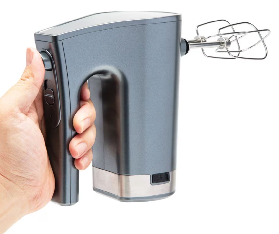 Trådløs håndmixer, metallic grå, med piskeris monteret, synlig hånd der holder produktet.