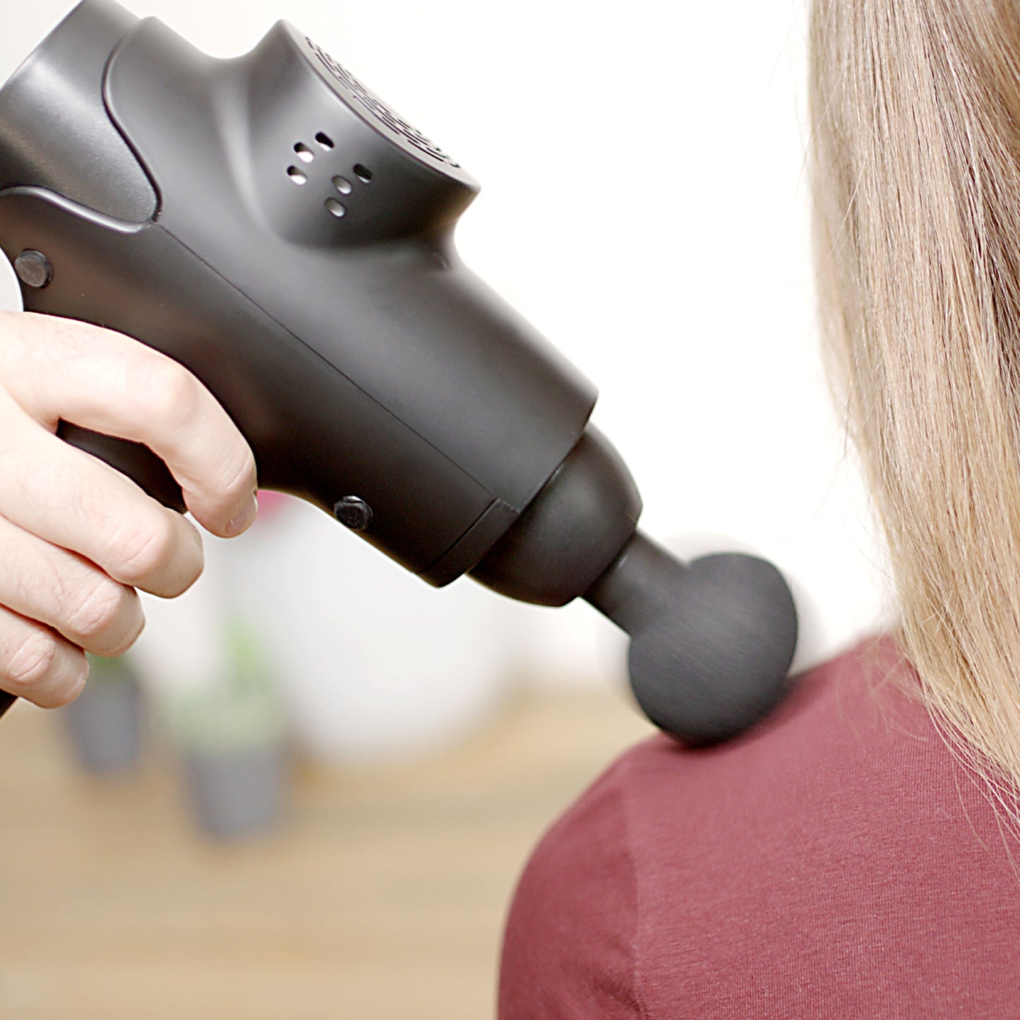 Rubicson Massagepistol USB-C med rundt massagehoved på skulder, person i bordeauxrød trøje.