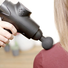 Rubicson Massagepistol USB-C med rundt massagehoved på skulder, person i bordeauxrød trøje.