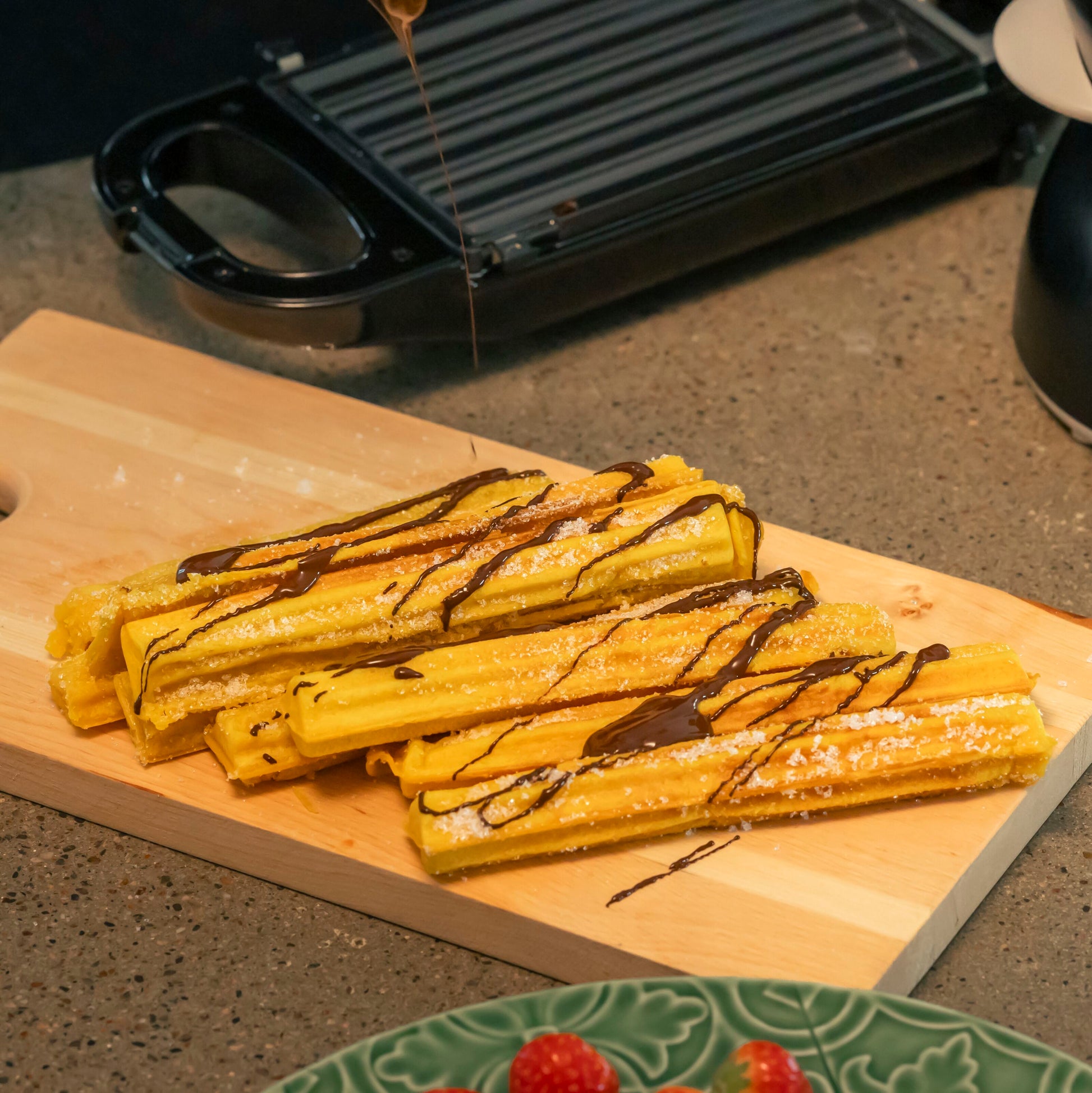 Fire sukkerdrysset churros med chokoladesovs på træbræt, Rubicson Churrosjern med nonstick-coating i baggrunden.