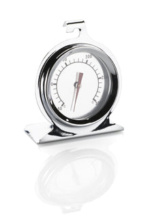 Analogt ovntermometer i rustfrit stål med krog og stativ, viser ca. 160°C, lad refleksion under termometeret.