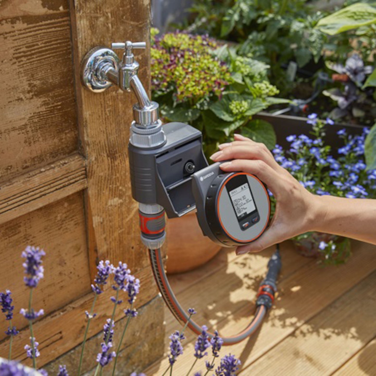 Gardena Flex vandingstimer justeres ved udendørs vandhane blandt blomster på træterrasse.