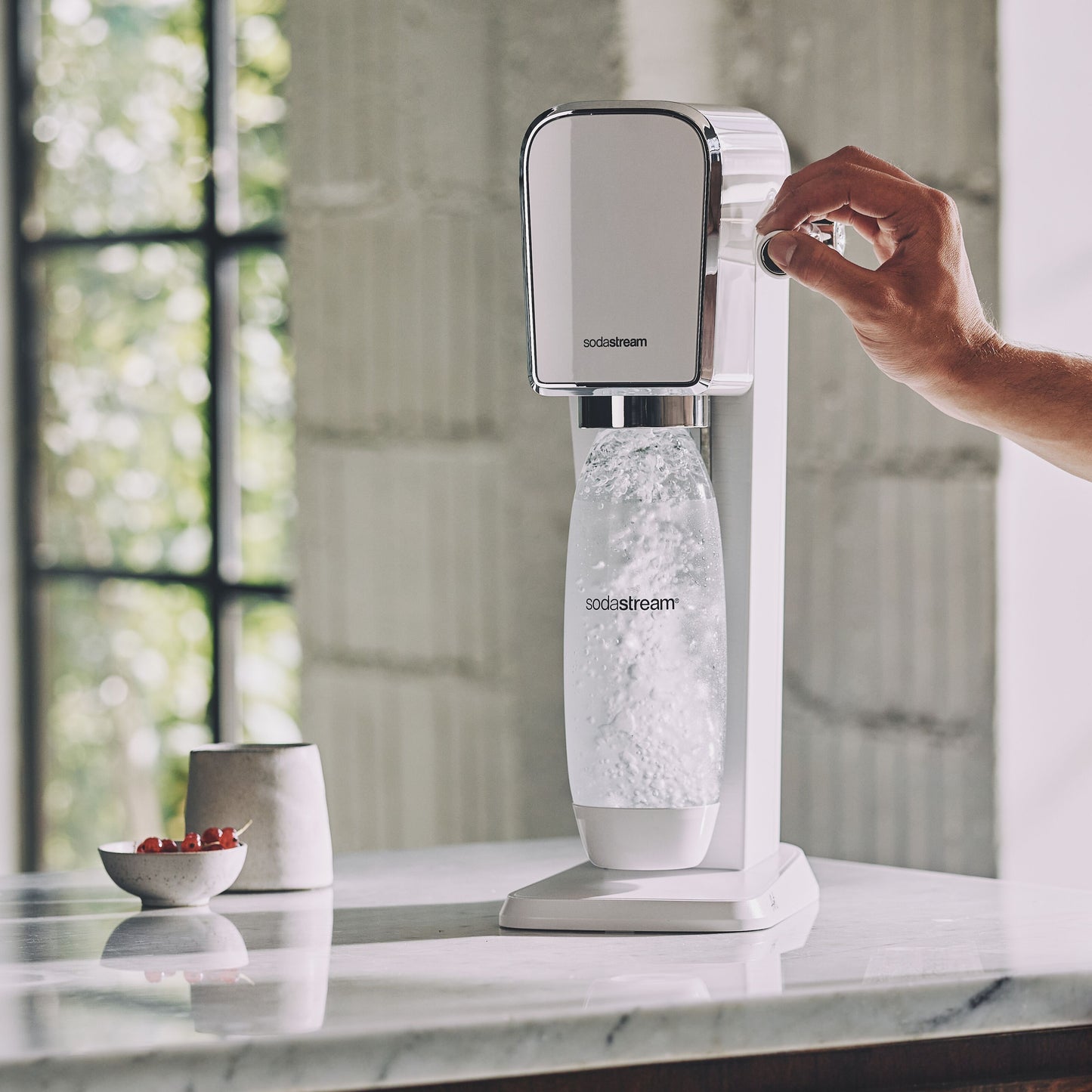 Sodastream sodavandsmaskine hånd drejer knap og laver danskvand i gennemsigtig flaske.