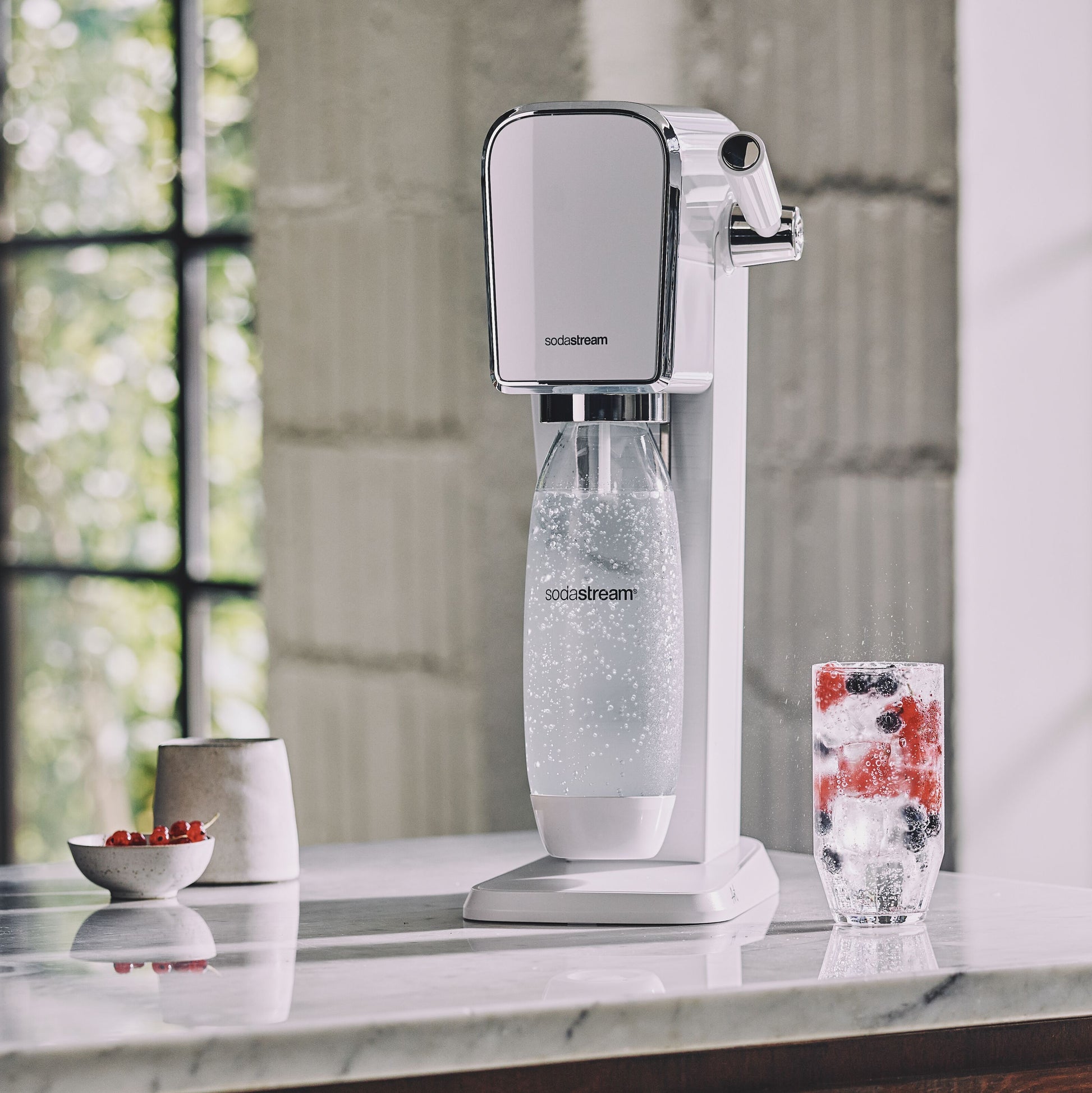 Sodastream sodavandsmaskine på marmorbord ved siden af glas med danskvand og bær.