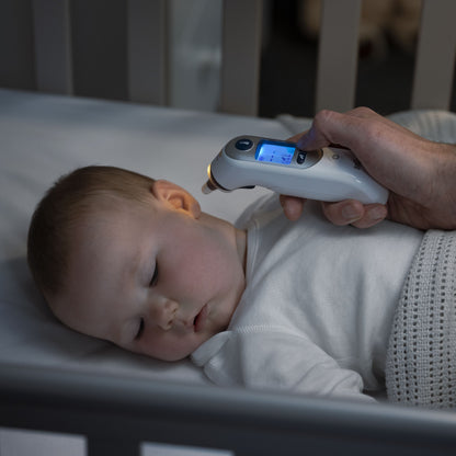 Braun Thermoscan 7+ Øretermometer bruges til at måle temperatur på baby i hvid sparkedragt og tæppe i tremmeseng.
