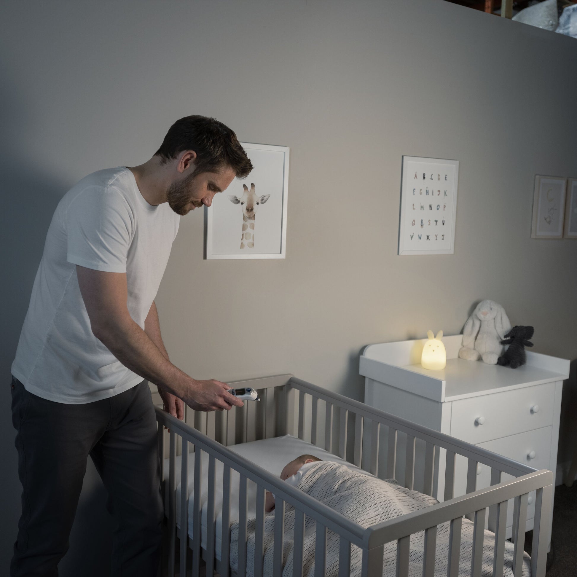 Braun Thermoscan 7+ Øretermometer bruges af mand ved tremmeseng med baby, hvid t-shirt, svagt lyst børneværelse.