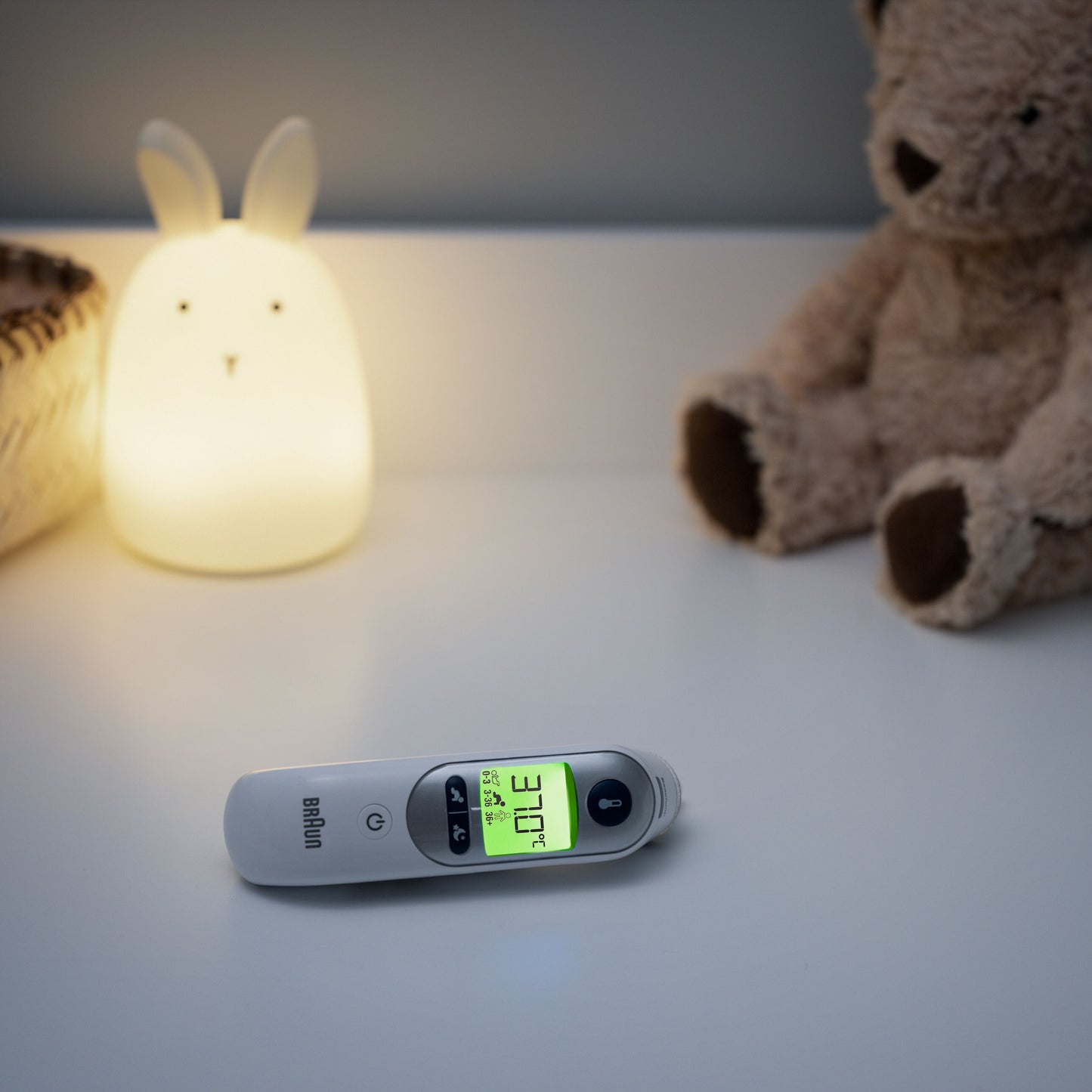 Braun Thermoscan 7+ øretermometer viser 37,0°C på bord ved siden af kaninformet natlampe og brun bamse.