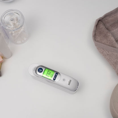 Braun Thermoscan 7+ øretermometer viser 37,0°C ved siden af vatpinde og sammenfoldet beige håndklæde.