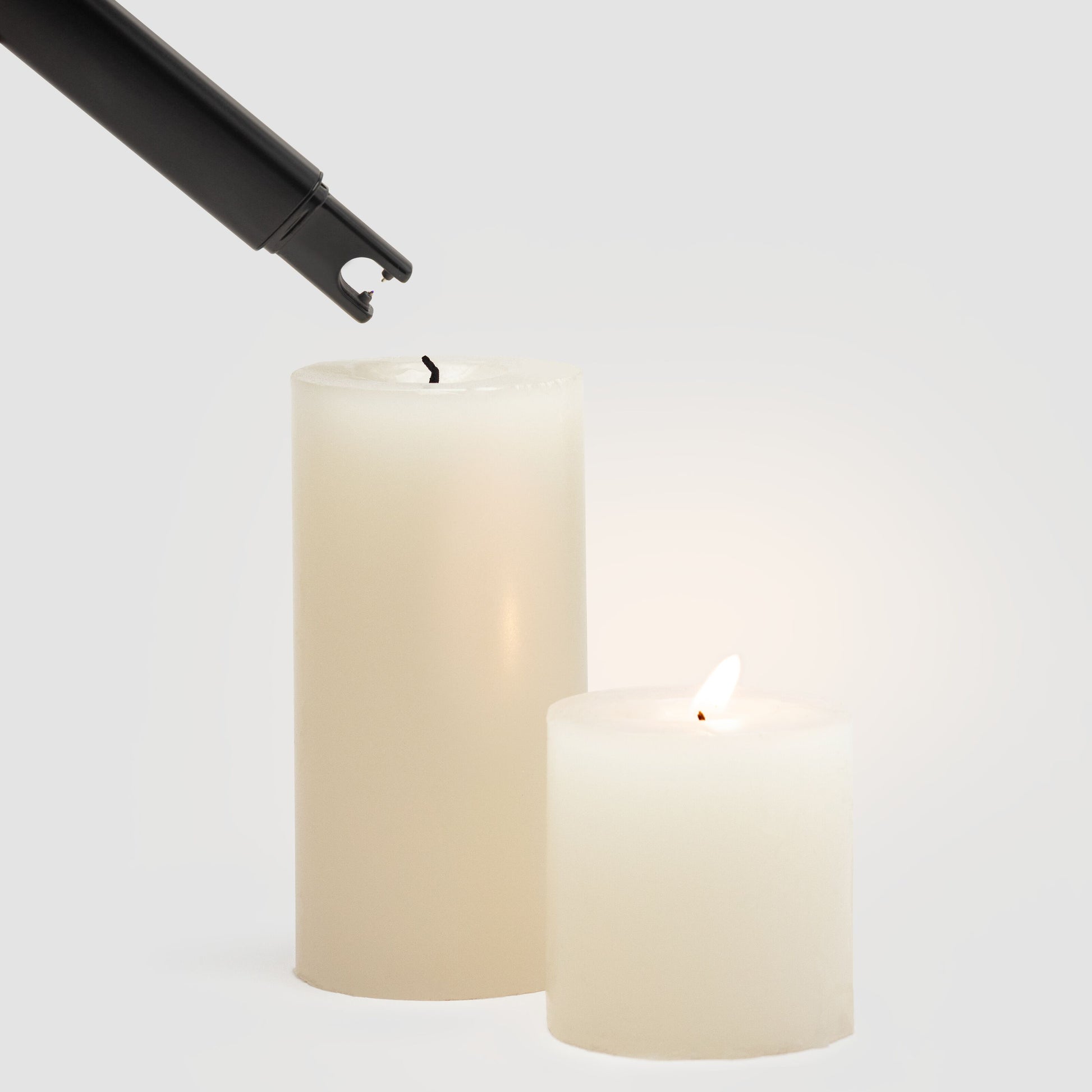 Sort Elektrisk lighter fra Rubicson tændes ved hvid lysestage, mindre hvidt stearinlys brænder ved siden af.