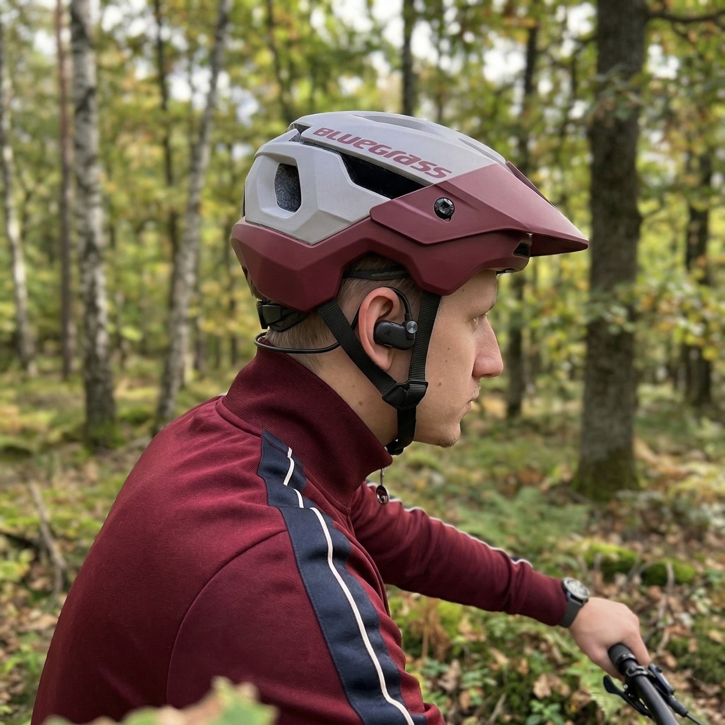 Nomadelic Solo 330 Sport open-ear-hovedtelefoner, rødbrun hjelm og jakke, vises udendørs.