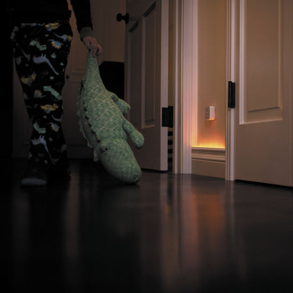 Philips Hue Motion sensor tænder orange natlys i mørk gang, barn i dinosaurpyjamas trækker bamsekrokodille.