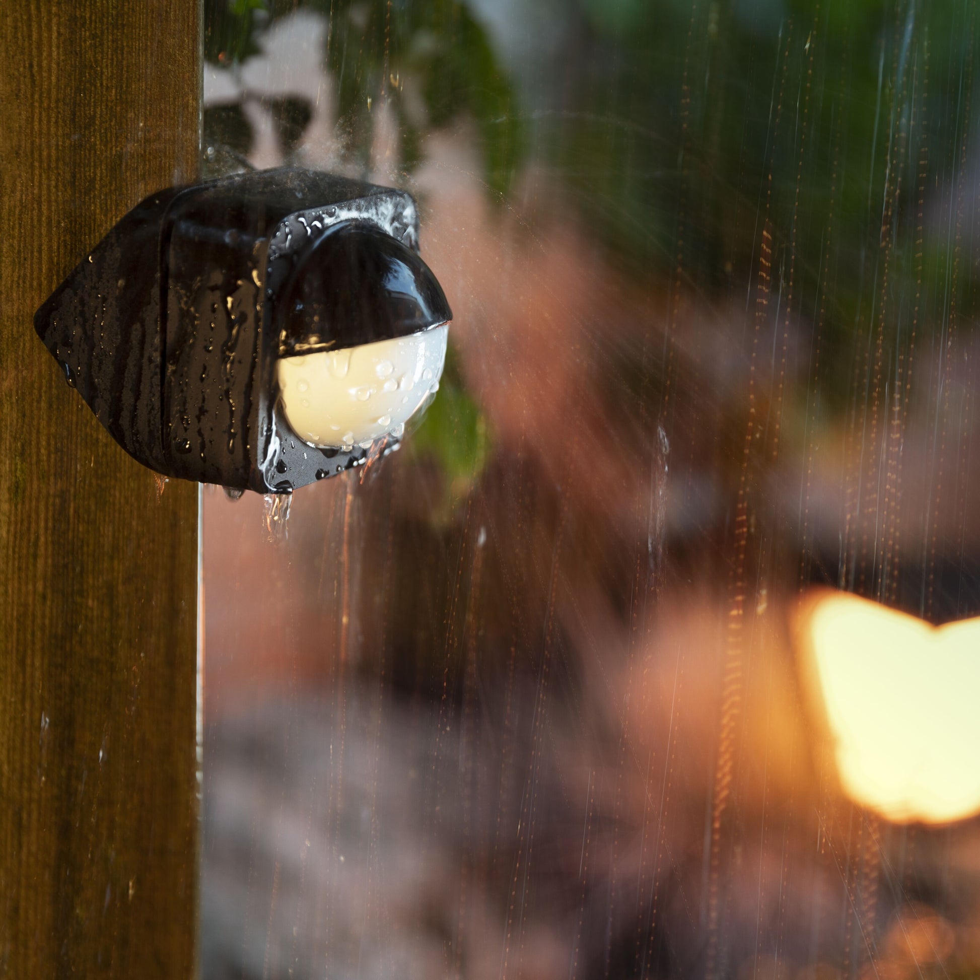 Philips Hue Bevægelsessensor til udendørs brug, våd med vanddråber, monteret på træstolpe i regn.