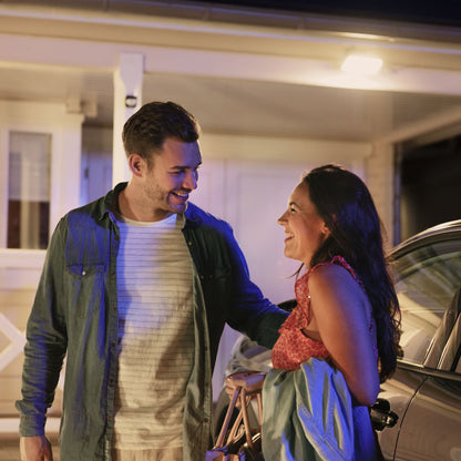 Philips Hue Bevægelsessensor til udendørs brug viser natlig belysning ved hus og bil, til personer synlige i lyset.