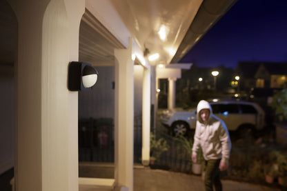 Philips Hue Bevægelsessensor udendørs installeret på søjle ved oplyst indgang, set i mørke.