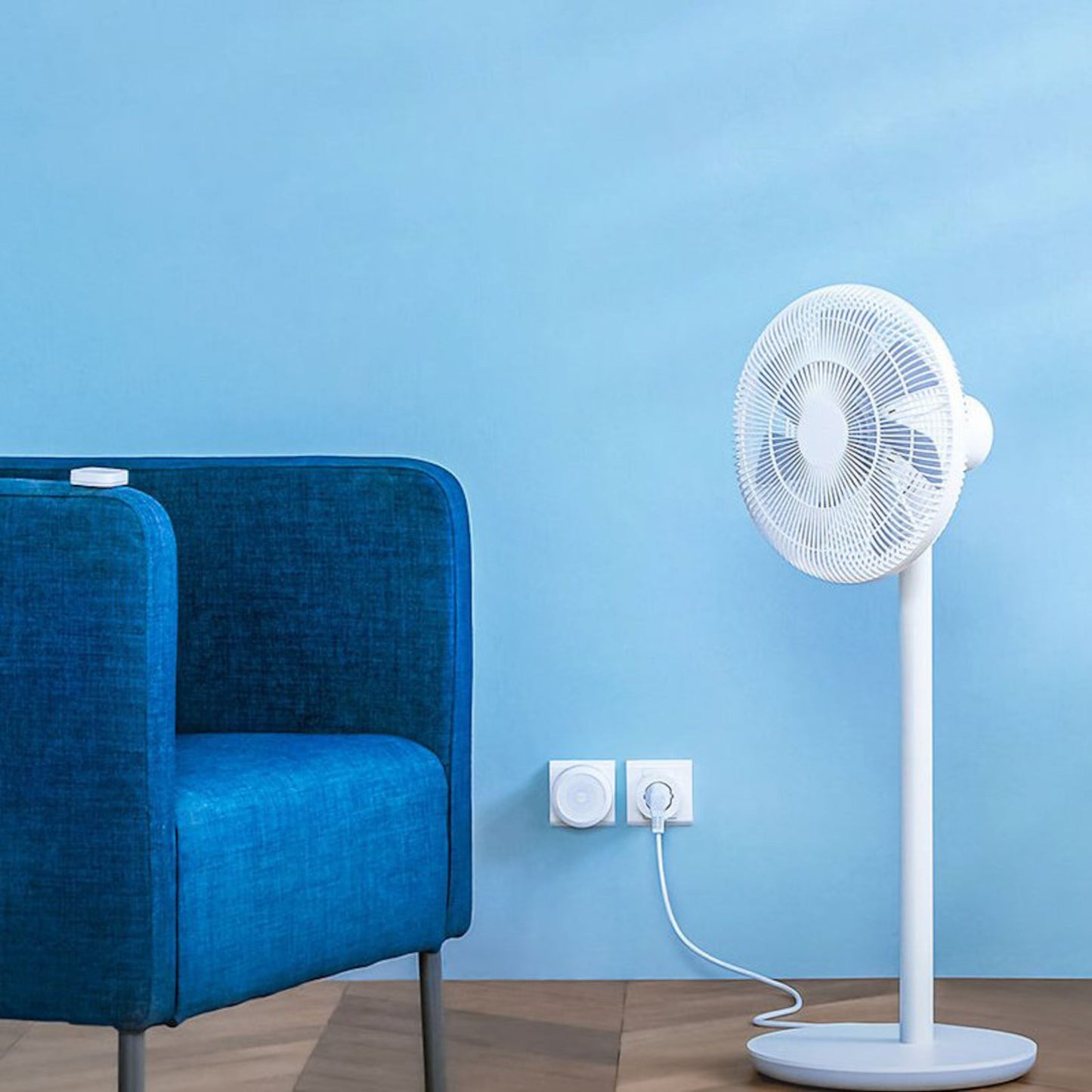 Aqara Smart stikprop til smart home styrer hvid standerventilator, synlig ved blå stol og blå væg, trægulv.