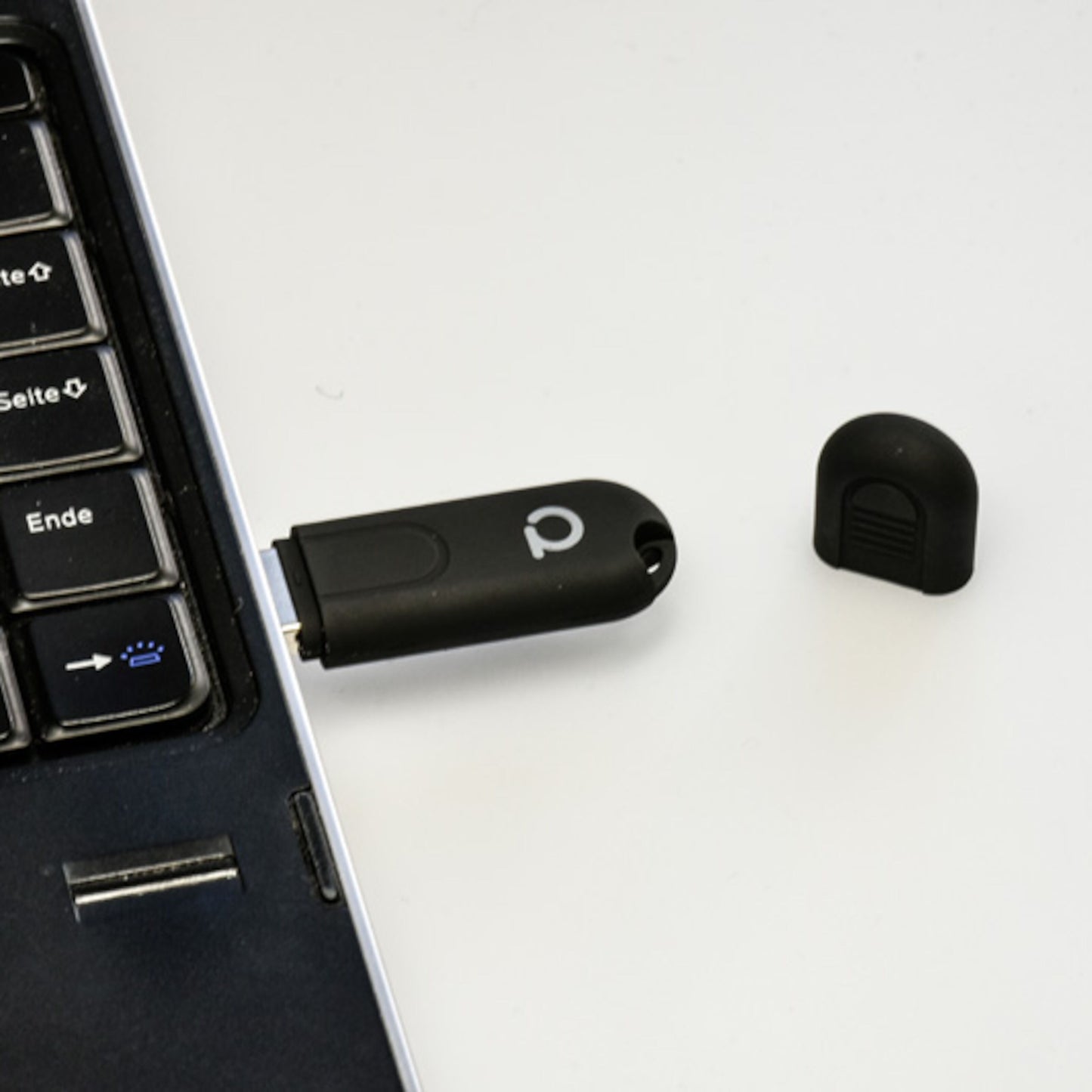 Conbee II Zigbee USB-controller sort, tilsluttet laptop med tyske tastaturtaster, hætte liggende ved siden af.