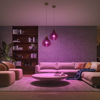 Philips Hue Color Ambiance LED-pære E27 1100 lm giver pink-lilla lys i stue med sofa og runde stole.