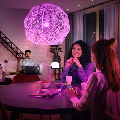 Hue Color Ambiance Startpakke Smarte LED-pærer synlige over bord med snacks i en stue, kvinder taler, mand arbejder.