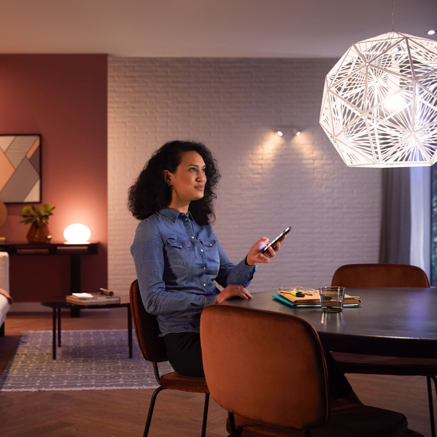 Hue Hvid Smart LED-pære E27 1100 lm monteret i pendel over spisebord, kvinde med smartphone, notesbog og glasvand.