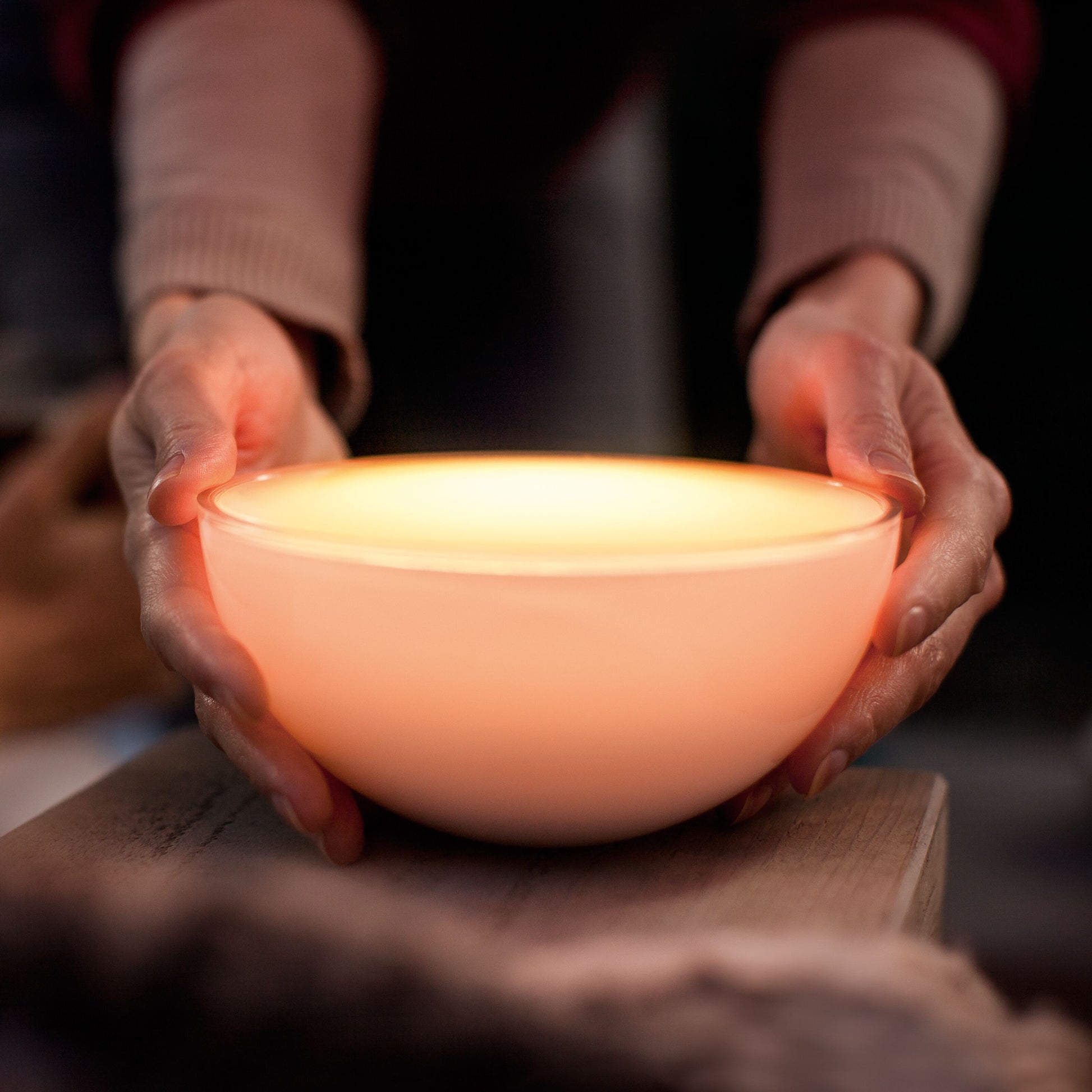 Philips Hue Go bærbar bordlampe afgiver varm ferskenfarvet lys, ses holdt med begge hænder.
