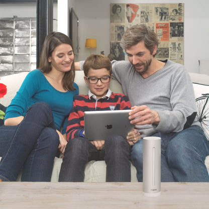 Netatmo Vejrstation Smart vejrstation på bord foran familie i stue, synlig tablet i brug, plakater og dekoration baggrund.