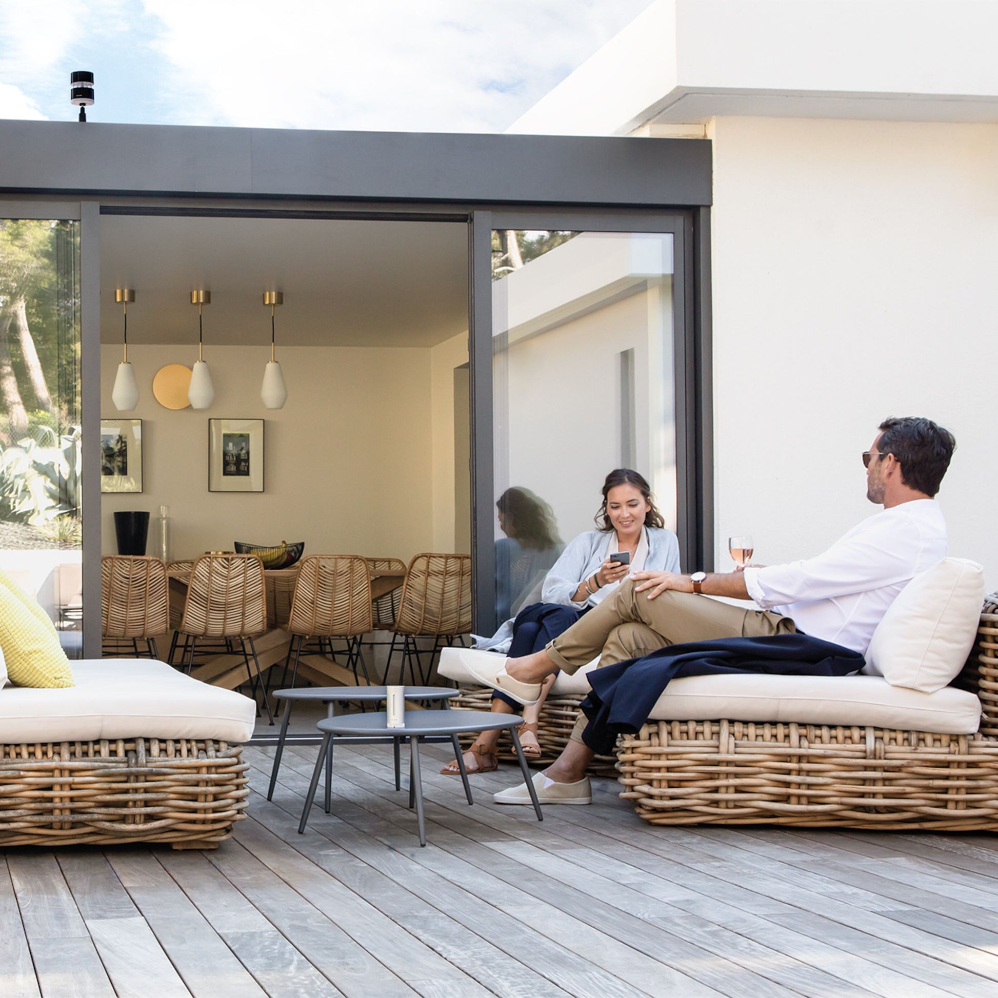 Netatmo Smart vejrstation app vist på telefon udendørs ved terrasse, moderne hus i baggrunden, loungeområde.