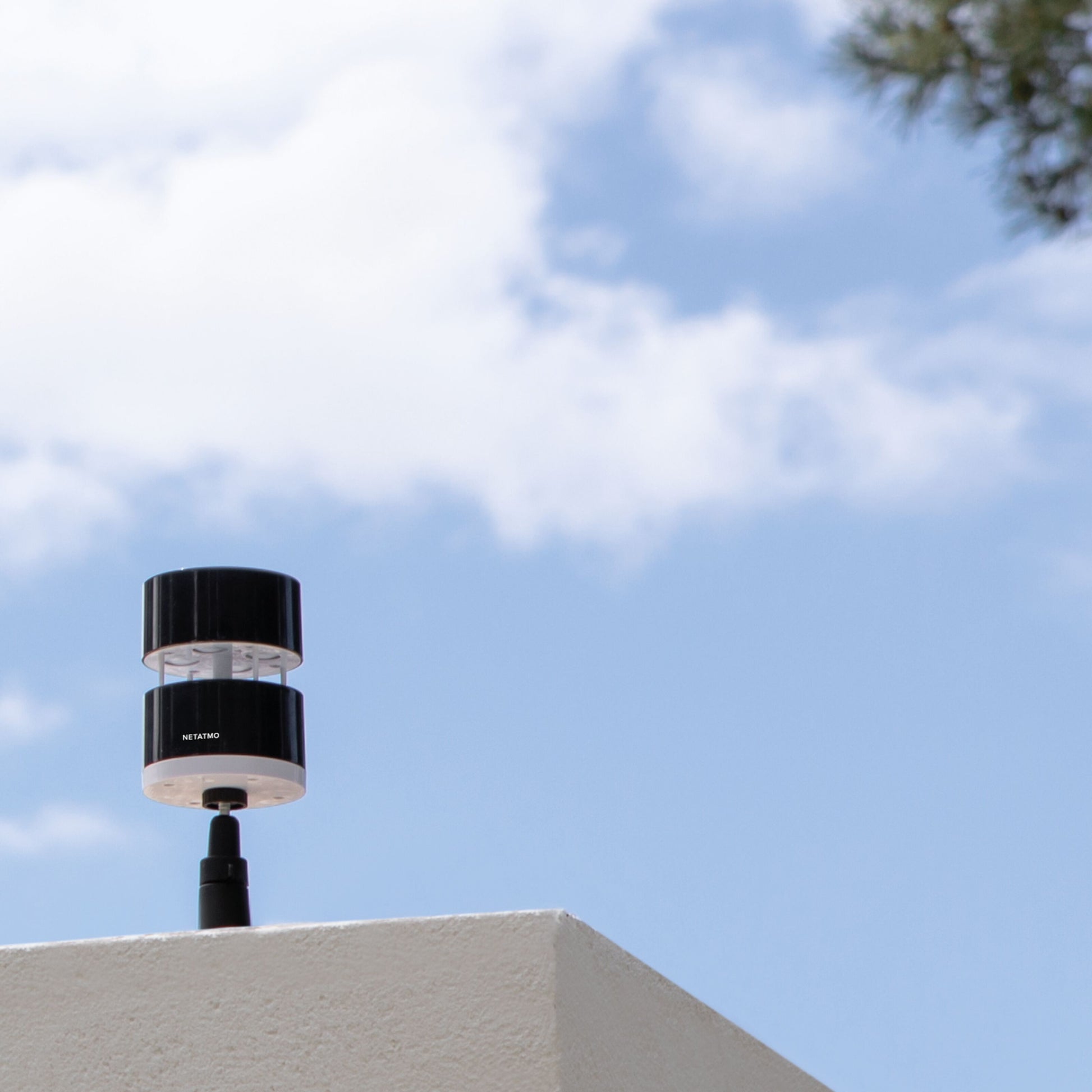 Netatmo Anemometer vindmåler til Netatmo vejrstation monteret på hvidt væg med blå himmel og skyer i baggrunden.