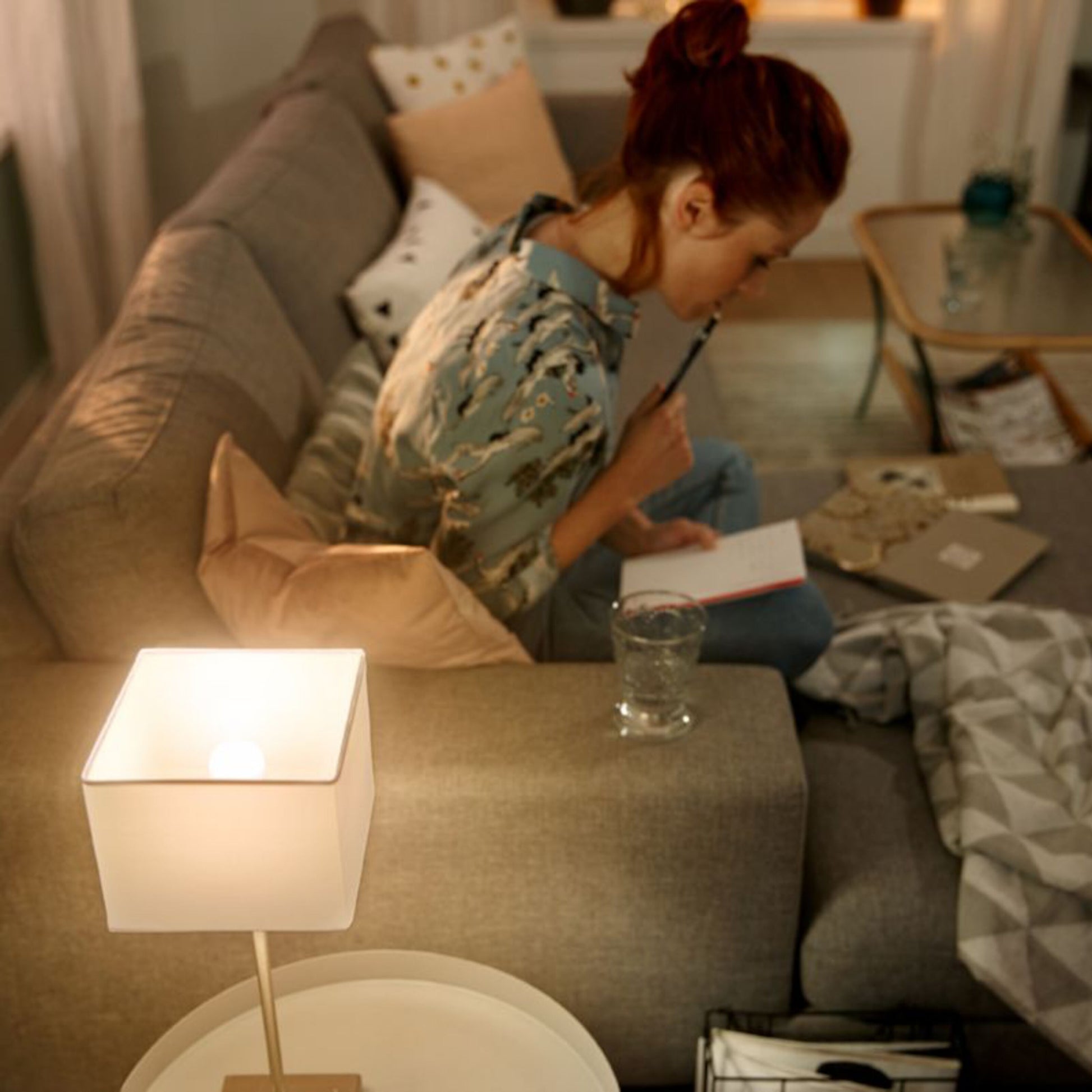 Hue Luster Smart LED-pære E14 470 lm lyser stue op, varm glød, grå sofa i baggrund.
