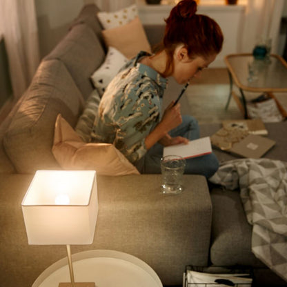 Hue Luster Smart LED-pære E14 470 lm lyser stue op, varm glød, grå sofa i baggrund.